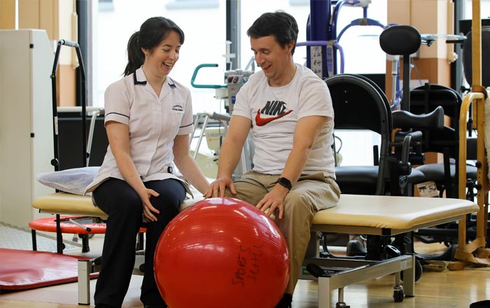 Female NRH staff member with male service user performing exercise with red yoga ball